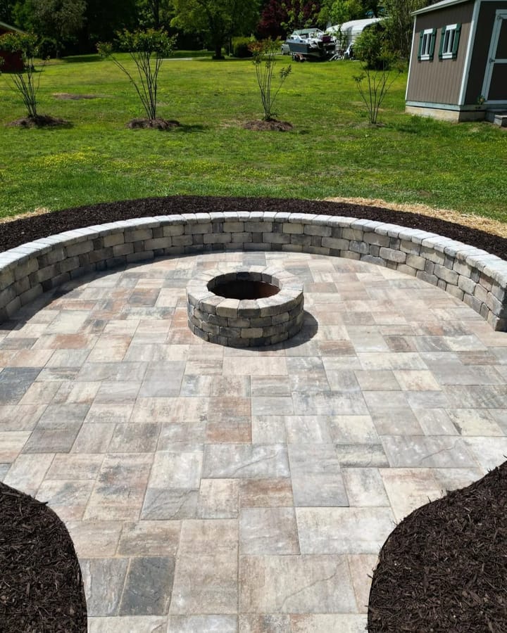 Stone fire pit in a circular paved seating area, with a curved block wall